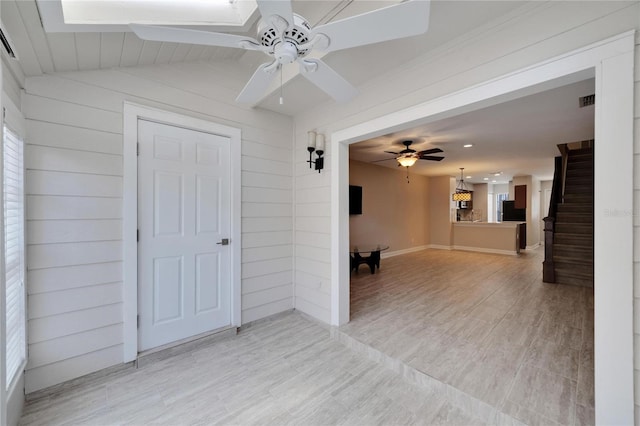 interior space with wooden walls, ceiling fan, and light wood-type flooring