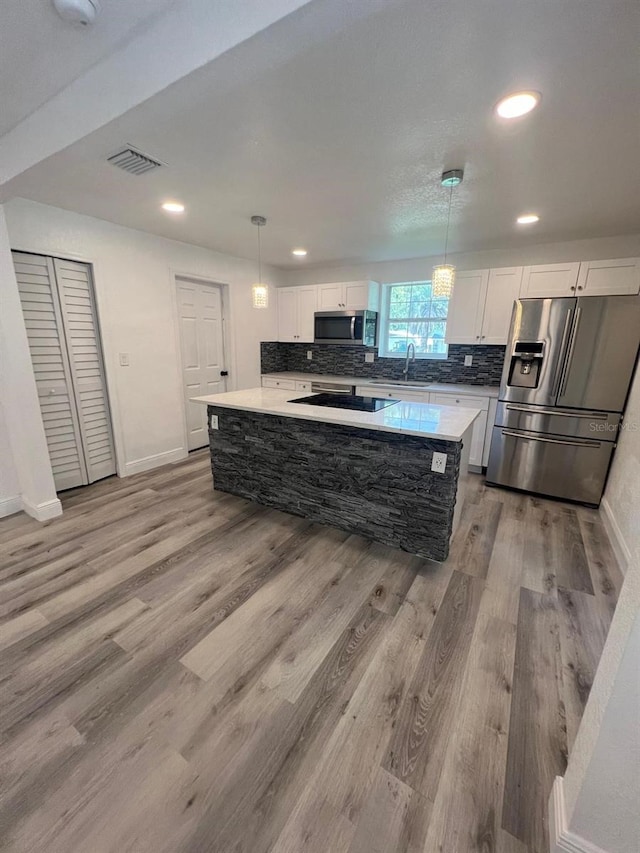 kitchen featuring appliances with stainless steel finishes, a kitchen island, white cabinets, pendant lighting, and backsplash