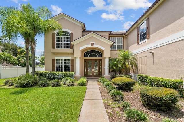 property entrance with stucco siding, fence, a lawn, and french doors