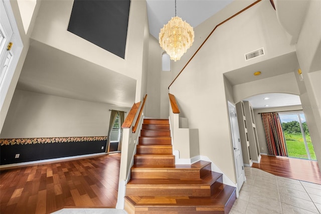 staircase featuring arched walkways, visible vents, a high ceiling, wood finished floors, and a chandelier