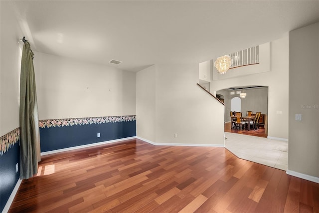 unfurnished room featuring arched walkways, a chandelier, wood finished floors, visible vents, and baseboards