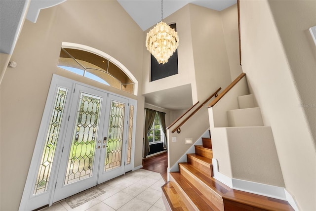 foyer entrance with a chandelier, high vaulted ceiling, light tile patterned flooring, baseboards, and stairway