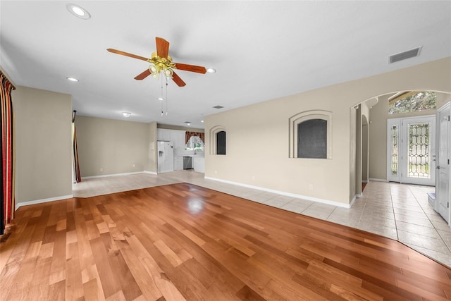 unfurnished living room featuring light wood-style flooring, visible vents, arched walkways, and a ceiling fan