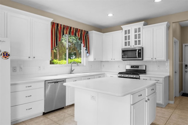 kitchen with stainless steel appliances, light countertops, glass insert cabinets, a sink, and a kitchen island