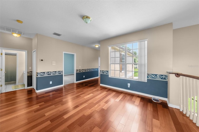 empty room with baseboards, a textured ceiling, visible vents, and wood finished floors