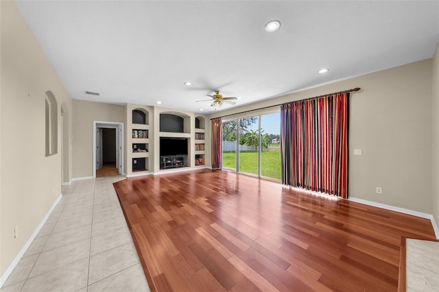 unfurnished living room with light wood finished floors, built in shelves, baseboards, and a fireplace with raised hearth