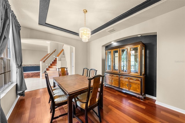 dining space with a chandelier, dark wood-style flooring, visible vents, baseboards, and a raised ceiling