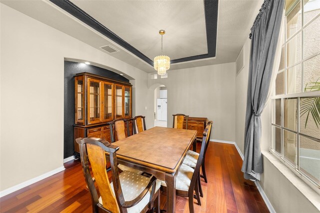 dining space featuring arched walkways, a tray ceiling, dark wood finished floors, and baseboards