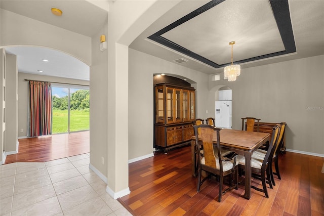 dining area featuring baseboards, arched walkways, visible vents, a raised ceiling, and wood finished floors