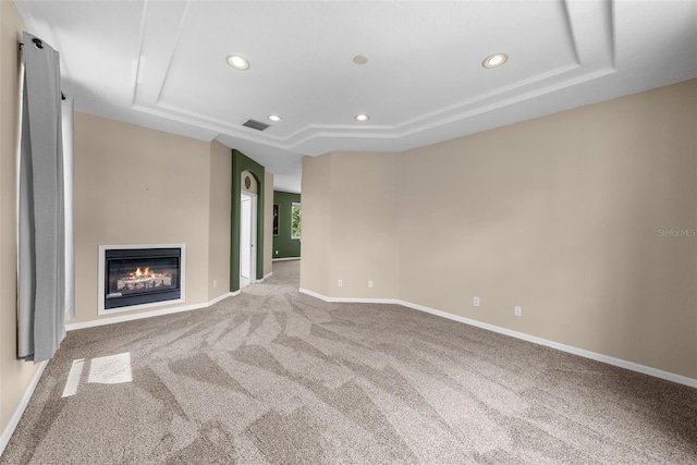 unfurnished living room with light carpet, baseboards, a glass covered fireplace, a tray ceiling, and recessed lighting