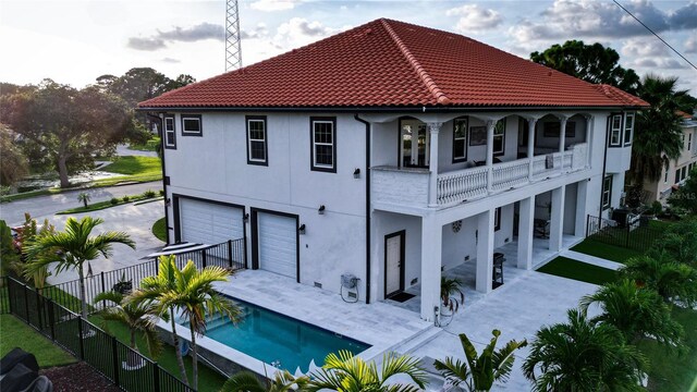 back of property featuring a balcony, a garage, and a fenced in pool