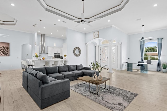 living room with a high ceiling, ornamental molding, ceiling fan, and a tray ceiling