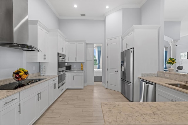 kitchen with ornamental molding, appliances with stainless steel finishes, white cabinets, and wall chimney exhaust hood