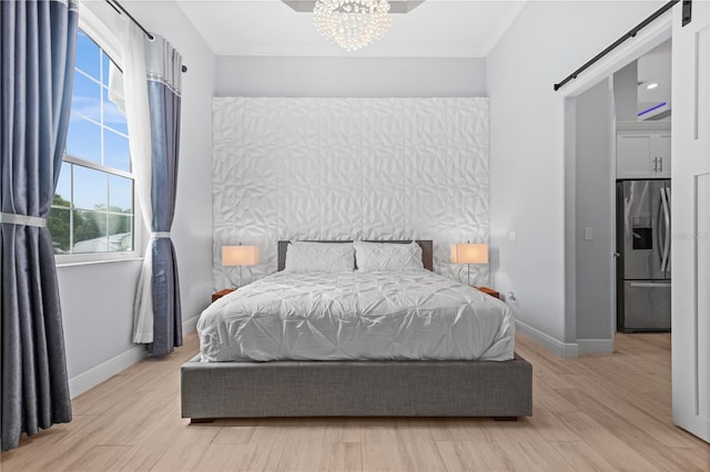 bedroom featuring an inviting chandelier, light wood-type flooring, ornamental molding, stainless steel fridge, and a barn door