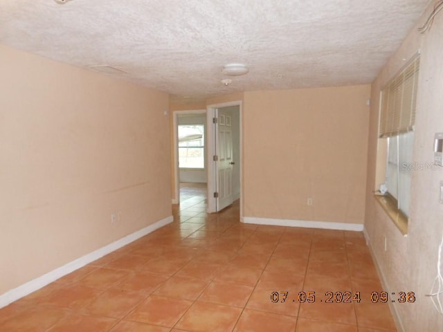 empty room with a textured ceiling, light tile patterned floors, and baseboards