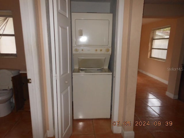 laundry area featuring baseboards, laundry area, tile patterned floors, and stacked washer / drying machine