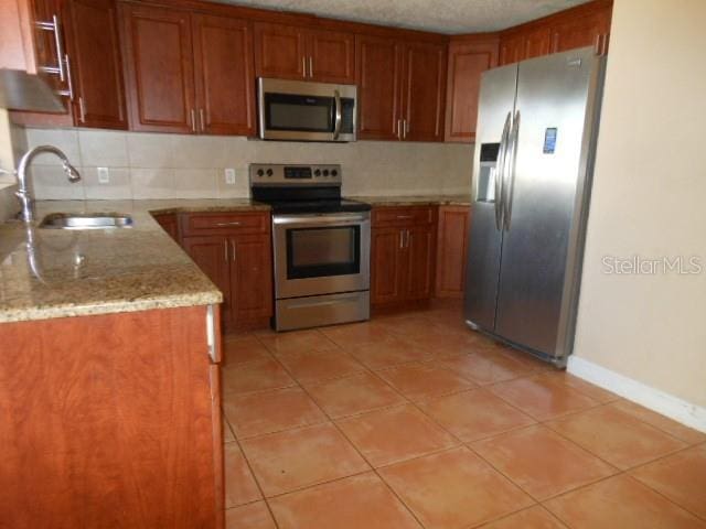 kitchen with stainless steel appliances, brown cabinetry, a sink, and light stone countertops