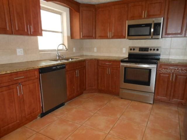 kitchen featuring decorative backsplash, appliances with stainless steel finishes, brown cabinets, a sink, and light tile patterned flooring