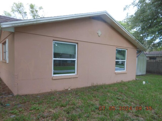 view of side of property featuring a yard, fence, and stucco siding