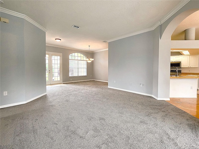 carpeted spare room with visible vents, crown molding, an inviting chandelier, arched walkways, and a sink