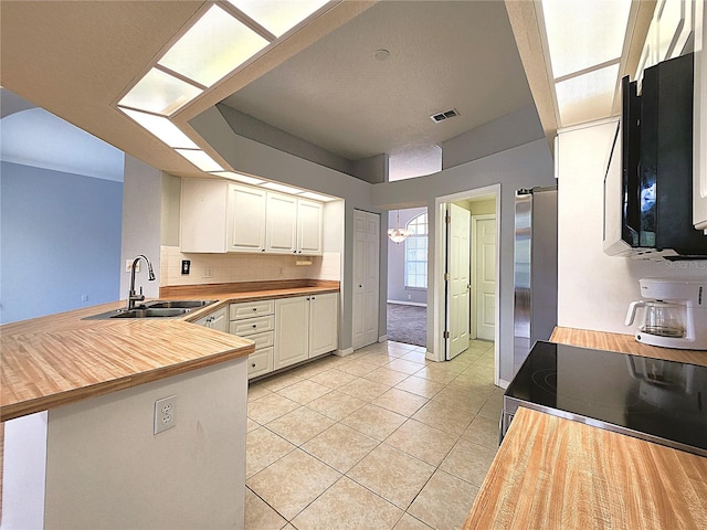 kitchen with sink, light tile patterned flooring, kitchen peninsula, decorative backsplash, and white cabinets