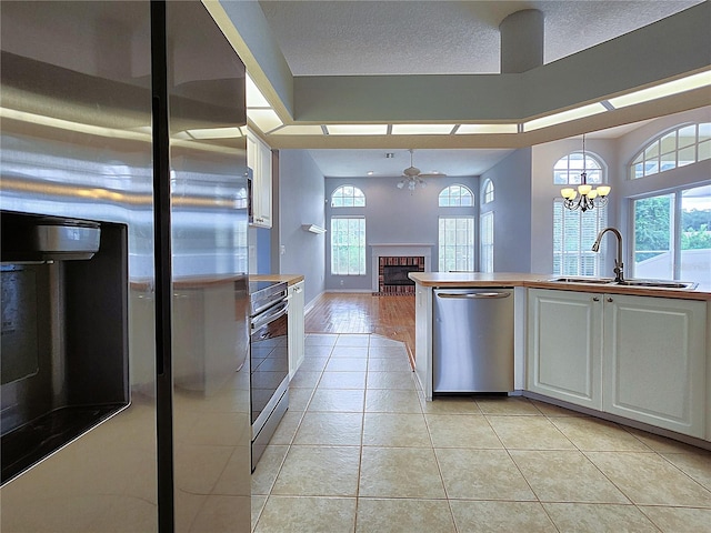 kitchen with a sink, white cabinetry, stainless steel appliances, light tile patterned flooring, and a fireplace