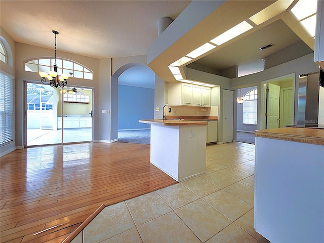 kitchen with hanging light fixtures, light tile patterned flooring, a notable chandelier, kitchen peninsula, and white cabinets