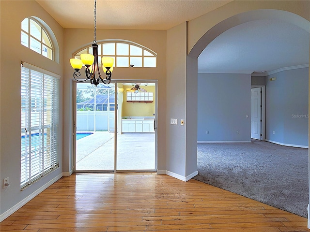 unfurnished dining area with ceiling fan with notable chandelier, light hardwood / wood-style flooring, and ornamental molding