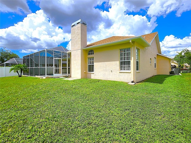 rear view of property with glass enclosure, a lawn, a chimney, and stucco siding