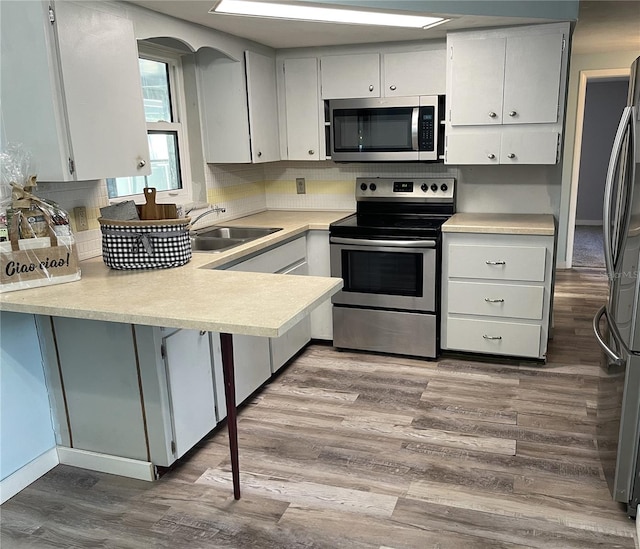 kitchen with sink, wood-type flooring, decorative backsplash, stainless steel appliances, and kitchen peninsula