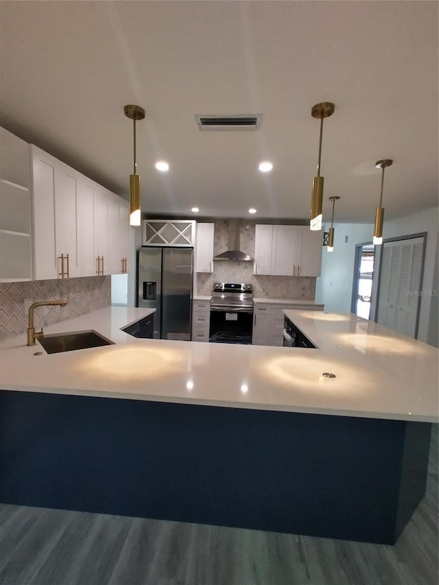 kitchen with white cabinets, appliances with stainless steel finishes, hanging light fixtures, and wall chimney range hood