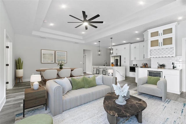 living room with ceiling fan, a raised ceiling, indoor wet bar, and light wood-type flooring