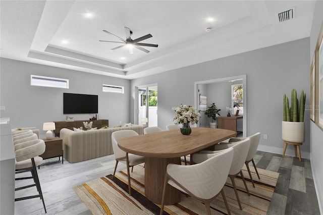 dining area with light hardwood / wood-style flooring, ceiling fan, and a tray ceiling