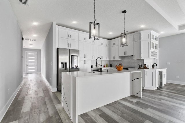 kitchen featuring stainless steel refrigerator with ice dispenser, pendant lighting, beverage cooler, a kitchen island with sink, and white cabinets