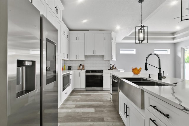 kitchen with hanging light fixtures, stainless steel appliances, white cabinets, and light stone countertops