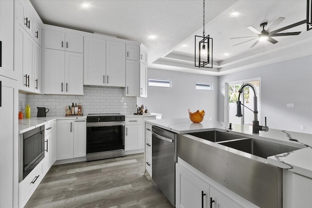 kitchen featuring a raised ceiling, appliances with stainless steel finishes, hanging light fixtures, and white cabinets