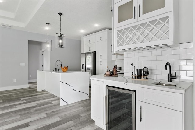 kitchen with wine cooler, sink, white cabinetry, hanging light fixtures, and light hardwood / wood-style flooring