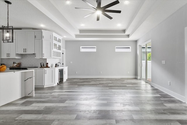 interior space with hanging light fixtures, a raised ceiling, white cabinets, decorative backsplash, and beverage cooler