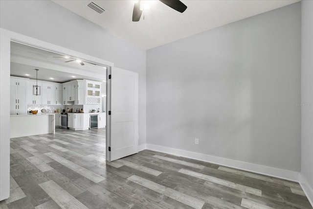 unfurnished room with wood-type flooring, wine cooler, and ceiling fan