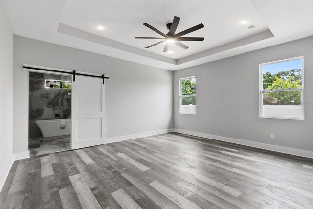 empty room featuring a raised ceiling, a barn door, ceiling fan, and light hardwood / wood-style flooring