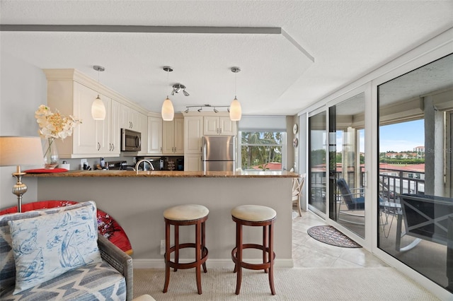 kitchen featuring kitchen peninsula, cream cabinets, stainless steel appliances, and decorative light fixtures