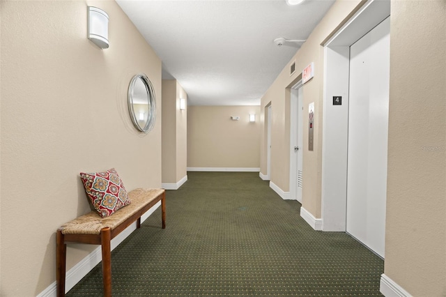 hall with dark colored carpet and elevator