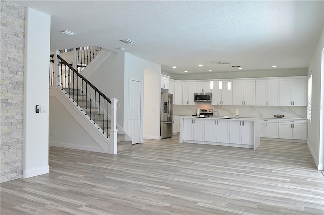 kitchen featuring decorative light fixtures, white cabinetry, stainless steel appliances, a kitchen island, and light hardwood / wood-style floors