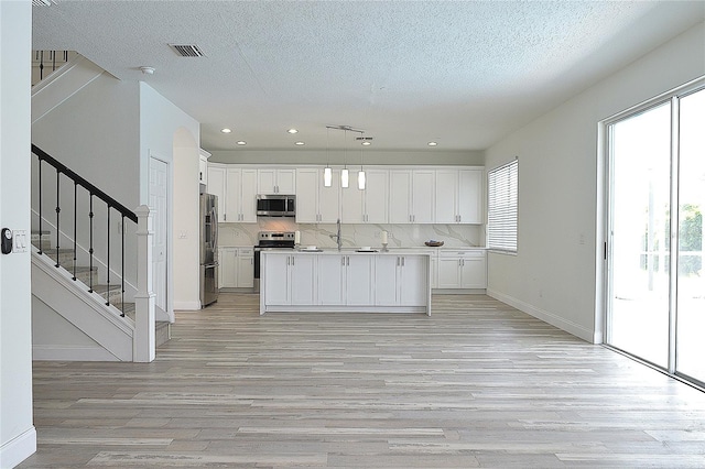 kitchen with white cabinetry, light wood-type flooring, stainless steel appliances, and decorative light fixtures