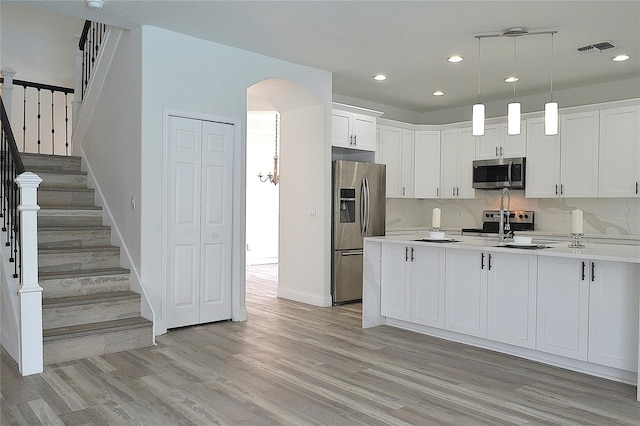 kitchen featuring light hardwood / wood-style flooring, stainless steel appliances, tasteful backsplash, hanging light fixtures, and white cabinetry