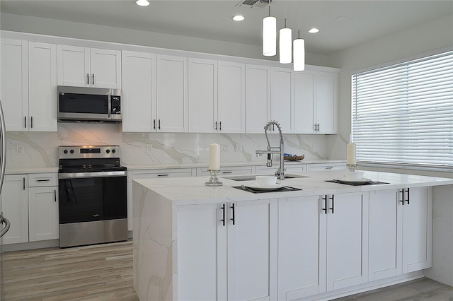 kitchen with white cabinetry, an island with sink, appliances with stainless steel finishes, light hardwood / wood-style flooring, and backsplash