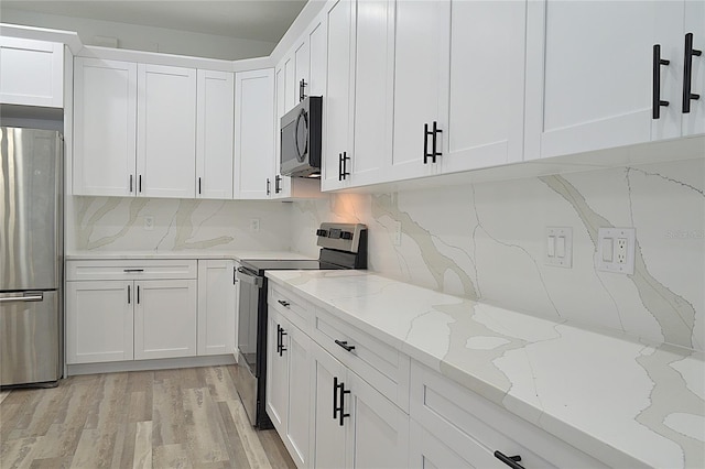 kitchen featuring tasteful backsplash, stainless steel appliances, white cabinets, light stone counters, and light hardwood / wood-style flooring