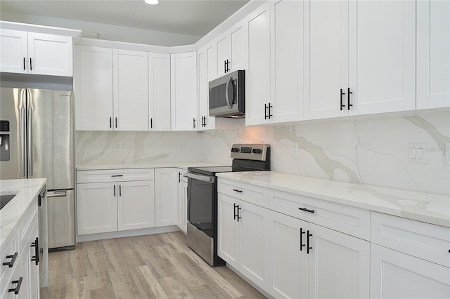 kitchen featuring white cabinetry, light stone countertops, light hardwood / wood-style floors, appliances with stainless steel finishes, and backsplash