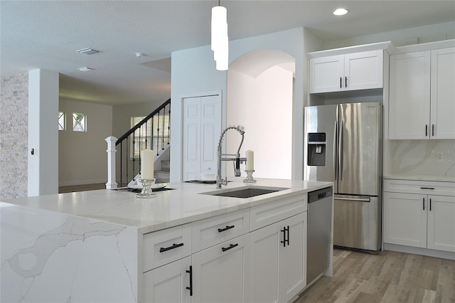 kitchen featuring light hardwood / wood-style flooring, light stone counters, hanging light fixtures, appliances with stainless steel finishes, and sink