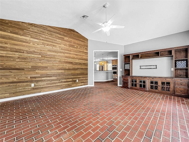 unfurnished living room with vaulted ceiling, ceiling fan, and wood walls